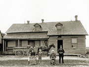 Family with horse and wagon in front of 1½-storey frame house.