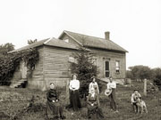 Family in front of 1½-storey frame house with one-storey wing.