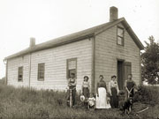 Family beside 1½-storey frame house.