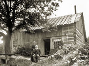 Elderly couple and younger man beside single-storey timber and board-sided house.