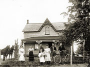 Family in front of 1½-storey stone house with centre gable.